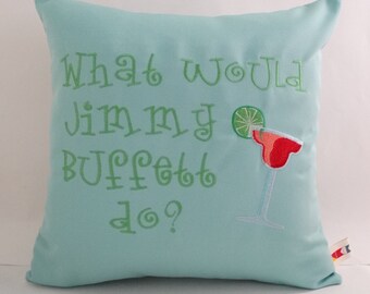 May include: A light blue throw pillow with the text "What would Jimmy Buffett do?" embroidered on it. A green lime wedge and a red margarita glass are also embroidered on the pillow.