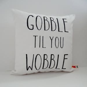 Może przedstawiać: Biała poduszka z czarnym tekstem, kt&oacute;ry brzmi "Gobble til you wobble".