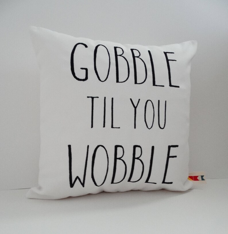 Może przedstawiać: Biała poduszka z czarnym tekstem, kt&oacute;ry brzmi "Gobble til you wobble".
