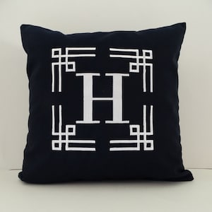 May include: A navy blue throw pillow with a white embroidered letter "H" in a geometric frame.