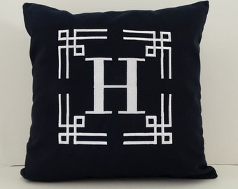 May include: A navy blue throw pillow with a white embroidered letter "H" in a geometric frame.