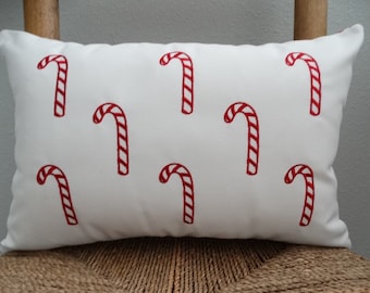 May include: White pillow with a red candy cane pattern. The pillow is rectangular and has a white background with red candy canes printed on it.