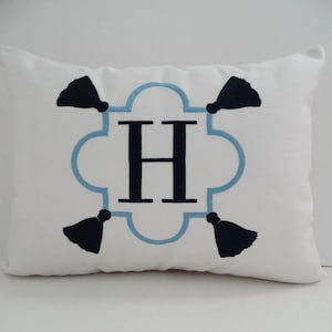 May include: White pillow with a blue and black embroidered monogram of the letter "H" in a decorative frame with tassels.