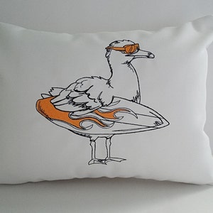 May include: White rectangular pillow featuring an embroidered cartoon seagull wearing orange sunglasses and holding an orange and white surfboard. The seagull is outlined in black. A small tag with a nautical flag design is attached to the side.