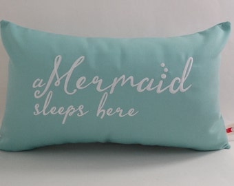 May include: A turquoise blue pillow with white embroidery that reads "a Mermaid sleeps here".