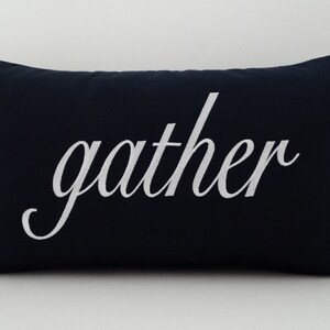 May include: A navy blue throw pillow with white embroidered text that reads "gather".