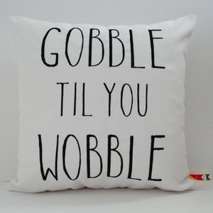 Może przedstawiać: Biała poduszka z czarnym tekstem, kt&oacute;ry brzmi "Gobble til you wobble".