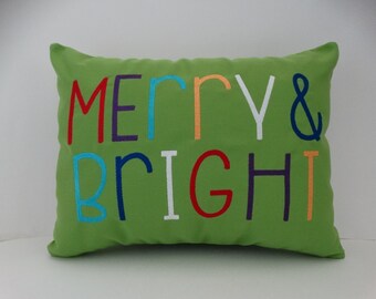 May include: Green throw pillow with the words "Merry & Bright" embroidered in colorful letters.