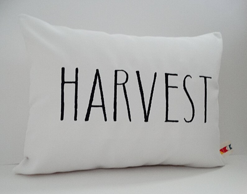Może przedstawiać: Biała poduszka z czarnym tekstem, kt&oacute;ry brzmi "HARVEST".