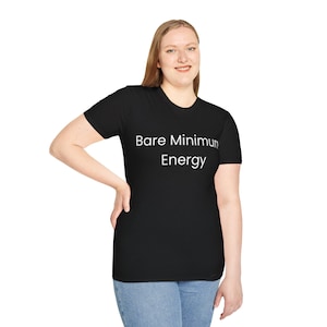 May include: Black t-shirt with the text "Bare Minimum Energy" in white. The shirt is a crew neck style and is being worn by a person. The person is wearing blue jeans.