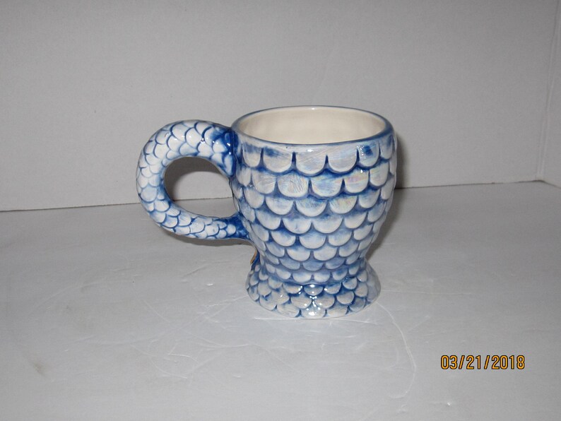 May include: A blue and white ceramic mug with a fishtail handle and a fish scale design.