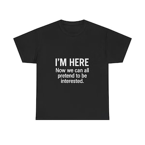 Puede incluir: Camiseta negra con el texto blanco "I'M HERE" encima del texto "Now we can all pretend to be interested." Una camiseta informal con cuello redondo.