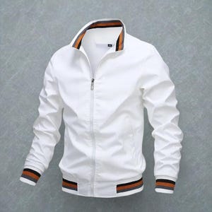 Könnte beinhalten: Weiße Bomberjacke mit durchgehendem Reißverschluss. Die Jacke hat ein gestreiftes Design in Braun-, Orange- und Grautönen an Kragen, Manschetten und Saum. Sie hat lange Ärmel und einen Stehkragen.