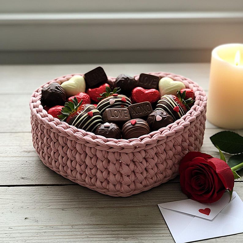 Pode incluir: Uma cesta rosa em forma de cora&ccedil;&atilde;o cheia de morangos cobertos com chocolate, chocolates e doces em forma de cora&ccedil;&atilde;o. Uma vela acesa, uma rosa vermelha e um envelope com um cora&ccedil;&atilde;o tamb&eacute;m est&atilde;o presentes.