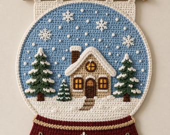 May include: A crochet wall hanging shaped like a snow globe featuring a light blue sky with white snowflakes, a tan house with a snow-covered roof, and two green pine trees. The base is dark red with white snowflake and berry embroidery.