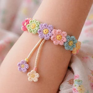 May include: A crochet bracelet with daisy-shaped flowers in various pastel colours, including pink, green, purple, and blue. The bracelet has a cream-coloured cord with two dangling flower charms. A delightful accessory.