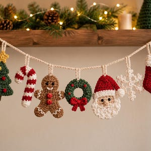 Op de afbeelding: Een gehaakte kerstslinger met zeven hangende ornamenten aan een crèmekleurig touw: een groene boom met een gele ster, een rood-witte zuurstok, een bruin peperkoekmannetje, een groene krans met een rode strik, een kerstmangezicht, een witte sneeuwvlok en een rode kerstsok.