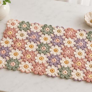 May include: A rectangular crochet mat constructed from numerous joined flower motifs in shades of sage green, dusty rose, lavender, and cream. Each individual flower features a central circular core surrounded by eight rounded petals.