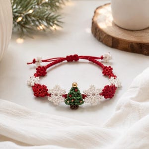 May include: A red adjustable cord bracelet featuring a central green crocheted Christmas tree with a gold bead topper, flanked by alternating white crocheted snowflakes and red crocheted flowers, with small white snowflake charms at the ends.