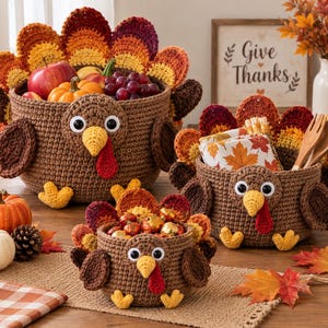 May include: Three brown crochet turkey baskets of varying sizes, each featuring a colorful fan-shaped tail, yellow beak, red wattle, and googly eyes. The baskets are filled with items including apples, grapes, a small pumpkin, and napkins.