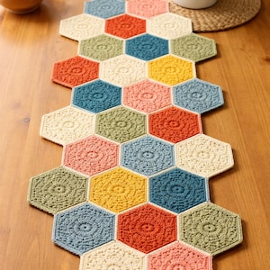 Könnte beinhalten: Handgehäkelter Tischläufer mit bunten sechseckigen Mustern. Die Farben umfassen Creme, Orange, Gelb, Blau und Grün. Jedes Sechseck hat ein detailliertes, kreisförmiges Muster, das eine strukturierte Optik erzeugt. Perfekt für die Tischdekoration.