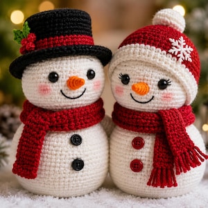 May include: Two crocheted snowmen figures with white bodies, orange carrot noses, and black bead eyes. The left snowman wears a black top hat with holly and a red scarf. The right snowman wears a red and white beanie with a snowflake and a red scarf.