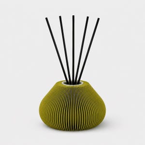 Pode incluir: Um difusor de cana decorativo com uma base de cerâmica canelada verde-amarelada e canas pretas. O vaso tem uma forma arredondada e bulbosa com uma abertura estreita no topo. As canas estão dispostas em forma de leque.