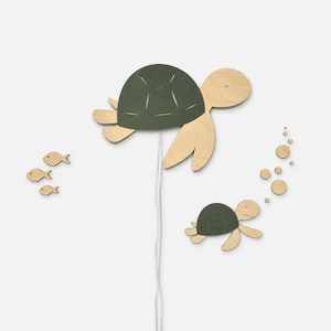 Può includere: Una decorazione da parete in legno raffigurante una grande tartaruga con guscio verde scuro e una tartaruga più piccola sottostante. Il set include tre piccole forme di pesce a sinistra e diverse bolle circolari che salgono dalla tartaruga piccola.