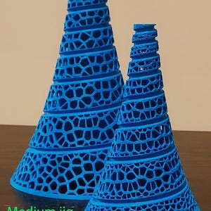 May include: Two blue, cone-shaped jigs with open, geometric designs. The larger jig has a base of 5.25 inches and a height of 8.25 inches. The smaller jig has a base of 3.25 inches and a height of 5.25 inches.