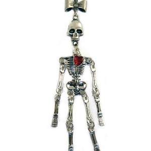 May include: A silver skeleton necklace with a red heart charm and a bow at the top.