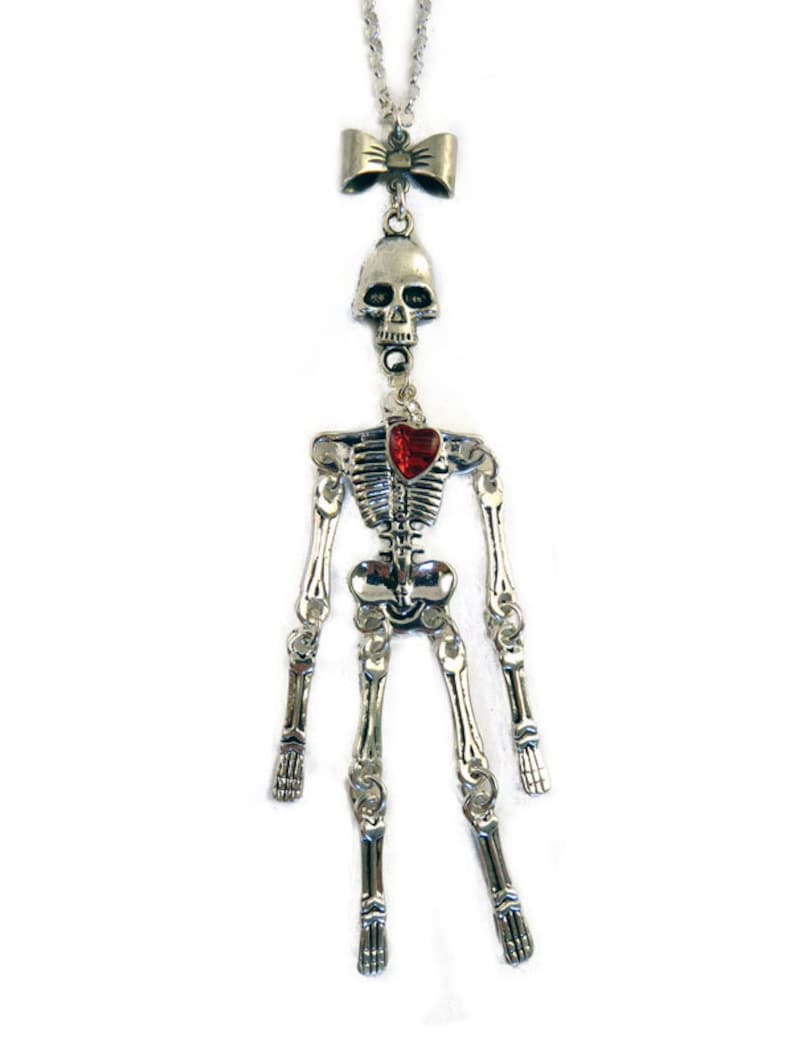 May include: A silver skeleton necklace with a red heart charm and a bow at the top.