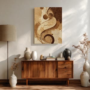 Op de afbeelding: Abstracte kunstprint met een wervelend ontwerp in bruine en beige tinten. Het kunstwerk bevat scriptachtige elementen en cirkelvormige vormen, waardoor een gelaagde en getextureerde uitstraling ontstaat. De print wordt weergegeven boven een houten kast met decoratieve vazen.