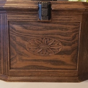 May include: A wooden box with a carved sunflower design on the front. The box has a hinged lid with a metal latch.