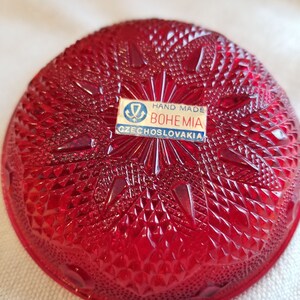 May include: A red glass bowl with a diamond pattern. The bowl has a label that reads "Hand Made Bohemia Czechoslovakia".