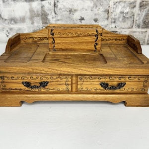 May include: A wooden jewelry box with two drawers and a top compartment. The box has a carved design and black metal drawer pulls.