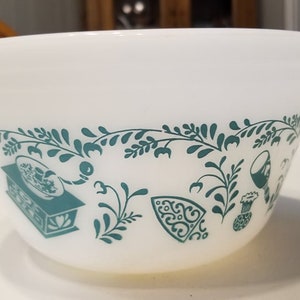 May include: White mixing bowl with a green floral design featuring a stylized iron, a pitcher, a wine glass, and a gramophone. The bowl is made of ceramic.
