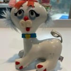 May include: A white plush toy cat with red hair, blue eyes, and a blue collar with a yellow buckle. The cat has white fur and pink ears.