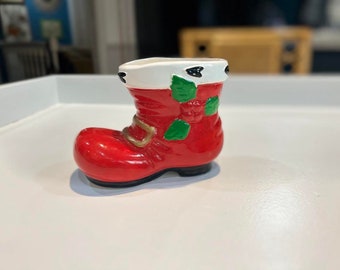 May include: A red and white ceramic Santa boot with green holly leaves. The boot is a planter or vase.