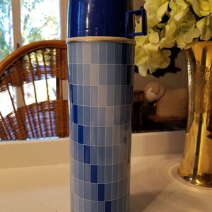May include: A blue and white Thermos brand vacuum insulated bottle with a blue lid and a carrying handle. The bottle has a checkered pattern.