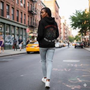 Könnte beinhalten: Ein schwarzer Kapuzenpullover mit dem Text "SPAGHETTI CODE" und "RUNS ON PRAY" in Rot und Weiß. Der Kapuzenpullover hat ein grafisches Design auf dem Rücken. Die Person trägt hellblaue Jeans und weiße Turnschuhe. Der Hintergrund ist eine Stadtstraße.