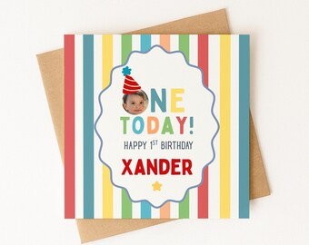May include: A square birthday greeting card with a colorful vertical striped background. The center features a scalloped white label with a photo of a child in a party hat, the text ONE TODAY! HAPPY 1ST BIRTHDAY, and the name XANDER in red.