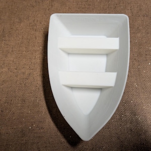 May include: A white, boat-shaped container with two rectangular, white dividers. The container has a smooth, matte finish and is set against a brown, textured background. The design is simple and modern.