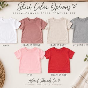 May include: A collection of six Bella+Canvas 3001T toddler t-shirts in white, heather mauve, heather dust, athletic heather, pink, and heather red. The text reads Shirt Color Options, Bella+Canvas 3001T Toddler Tee, and Adored Threads Co.