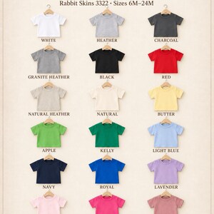 May include: A color chart for Rabbit Skins 3322 infant tees in sizes 6M-24M, featuring 18 short-sleeve shirts on hangers in white, heather, charcoal, granite heather, black, red, natural heather, natural, butter, apple, kelly, light blue, navy, royal, lavender, pink, hot pink, and mauvelous.