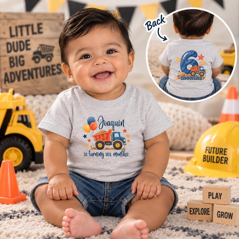 May include: A light gray short-sleeve t-shirt featuring a graphic of a dump truck, balloons, and the text 'Joaquin is turning six months' on the front, with a matching graphic on the back showing a large number six and the word 'months'.