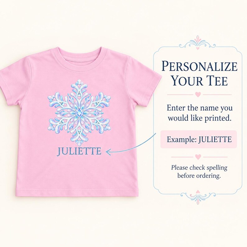 May include: A light pink short-sleeved t-shirt featuring a large, intricate blue and white snowflake graphic centered on the chest. Below the snowflake, the name JULIETTE is printed in blue. To the right, text reads: PERSONALIZE YOUR TEE.