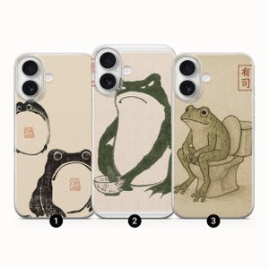 以下が含まれることがあります： 3つのカエルイラストが描かれたスマホケース。最初のケースは、円形のデザインの黒いカエルが特徴です。2番目のケースは、ボウルを持っている緑色のカエルです。3番目のケースは、日本語のテキストが入ったトイレにいるカエルを示しています。