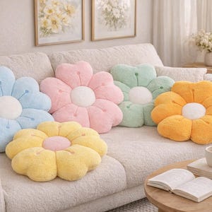 May include: Five flower-shaped cushions in pastel shades of blue, pink, green, yellow, and orange. Each cushion has a white centre. The cushions are arranged on a cream-coloured sofa, creating a cheerful and inviting atmosphere.