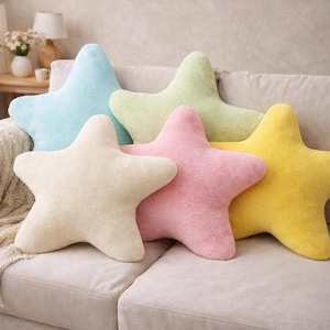 May include: Five star-shaped cushions in pastel shades of blue, green, cream, pink, and yellow. The cushions are arranged on a neutral sofa, creating a soft and inviting aesthetic. These decorative cushions add a whimsical touch to any room.