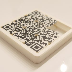 May include: A white puzzle with a QR code design. The puzzle is made of several small pieces that fit together to form the complete code. The black and white code is partially assembled, with a section missing.